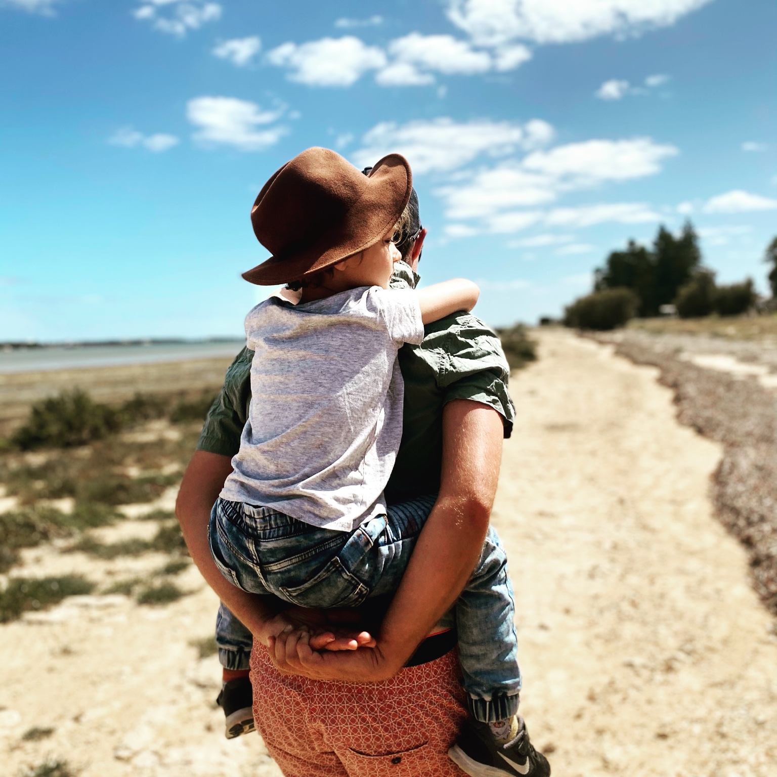 Greg giving Channing a piggyback along a sunlit coastal path